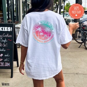 A person wearing a white t-shirt with a colorful graphic design on the back is walking on a sidewalk.