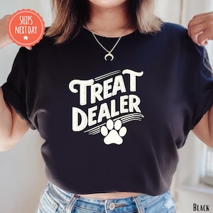 K&ouml;nnte beinhalten: Schwarzes T-Shirt mit dem Text "Treat Dealer" in wei&szlig;er, stilisierter Schrift und einem wei&szlig;en Pfotenabdruck. Das Shirt hat einen Rundhalsausschnitt und kurze &Auml;rmel. Der Text "Ships Next Day" befindet sich in einem roten Kreis.