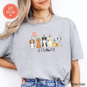 A woman wearing a gray t-shirt with a graphic of a group of dogs wearing party hats and the text "Let's Pawty!"