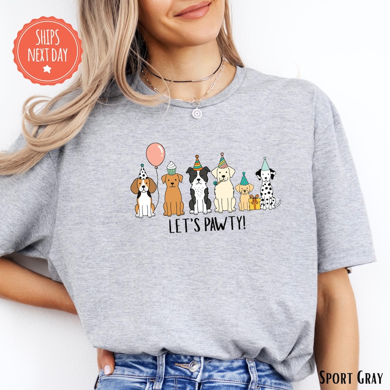 A woman wearing a gray t-shirt with a graphic of a group of dogs wearing party hats and the text "Let's Pawty!"
