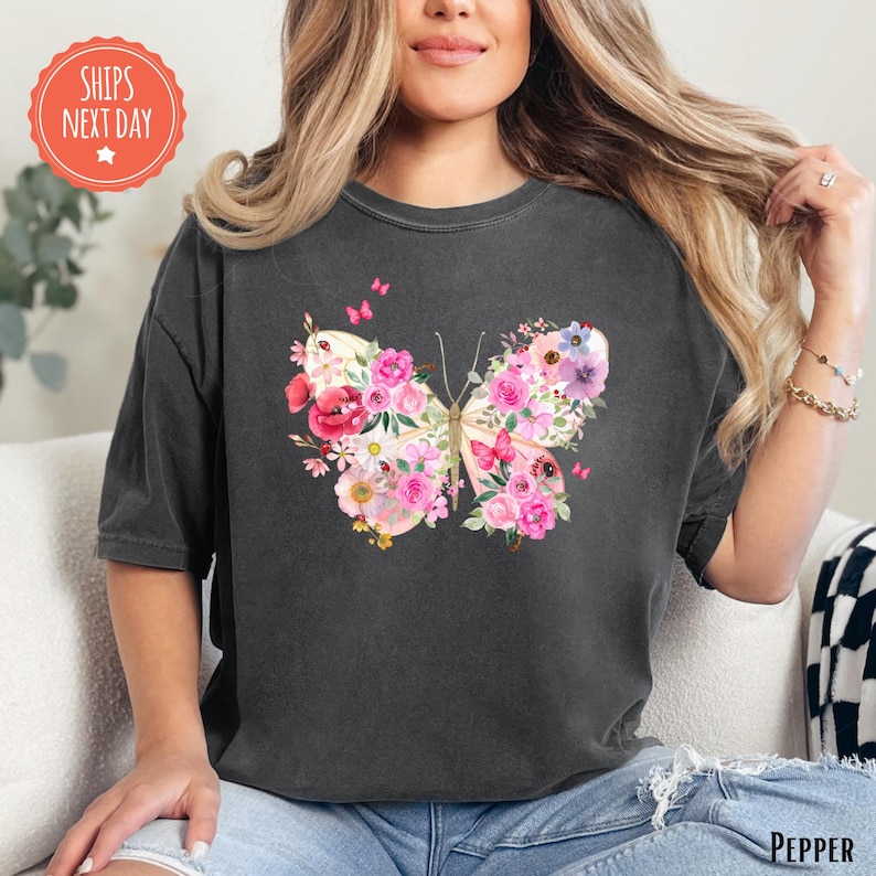 A woman wearing a black t-shirt with a colorful butterfly design featuring pink and white flowers.