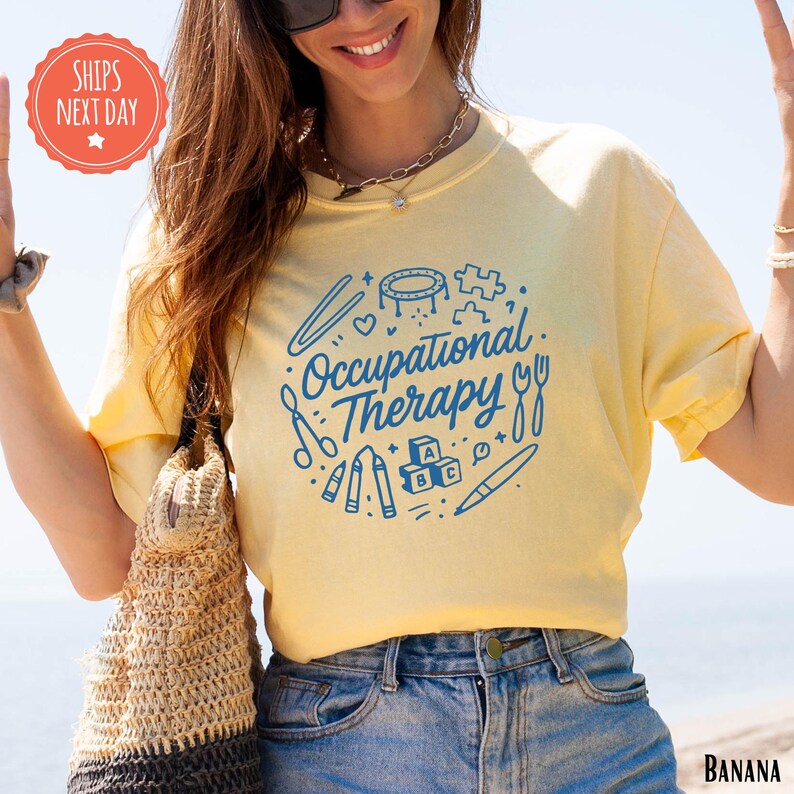 A woman wearing a yellow t-shirt with the text "Occupational Therapy" printed on it, smiling and holding a woven bag.