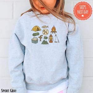 a little girl wearing a sweatshirt with camping icons on it