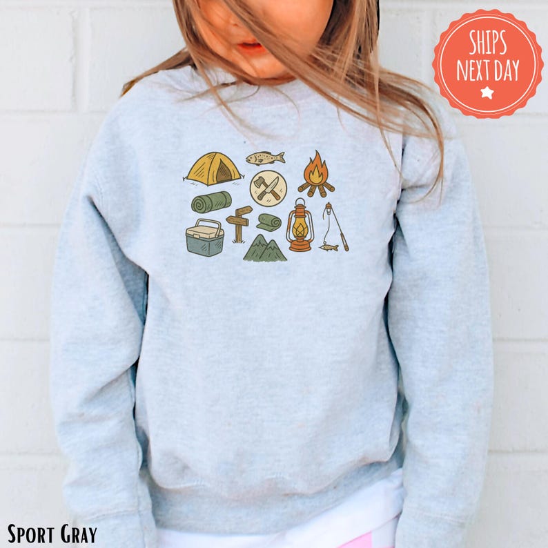 a little girl wearing a sweatshirt with camping icons on it