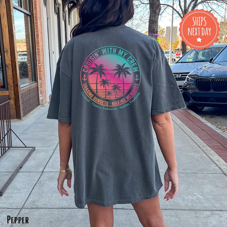 A person wearing a gray t-shirt with a colorful graphic design on the back, standing on a sidewalk next to a building.