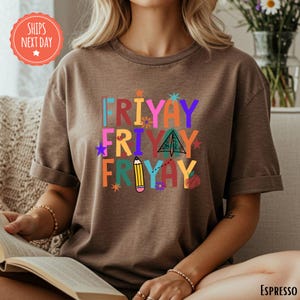A woman is sitting on a couch, reading a book, wearing a brown t-shirt with a colorful graphic design.