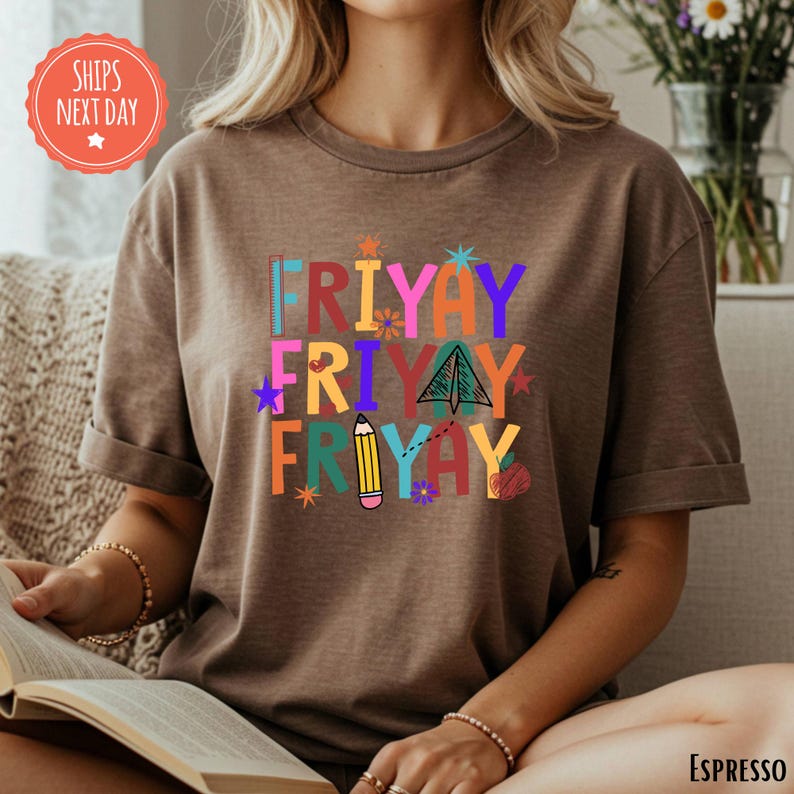 A woman is sitting on a couch, reading a book, wearing a brown t-shirt with a colorful graphic design.