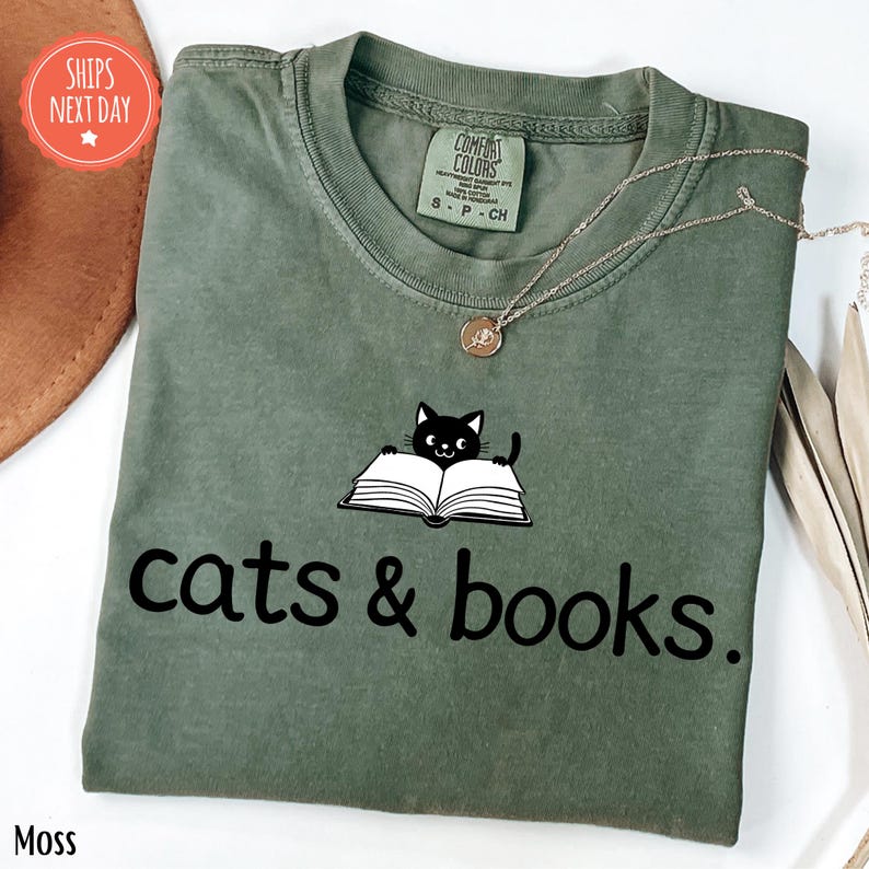 a green shirt with a cat and books on it