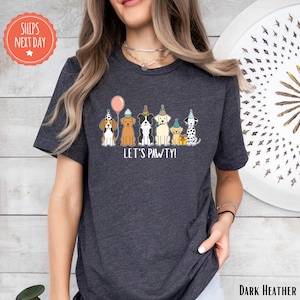 A woman wearing a gray t-shirt with a graphic design of five dogs wearing party hats and the text "Let's Pawty!"