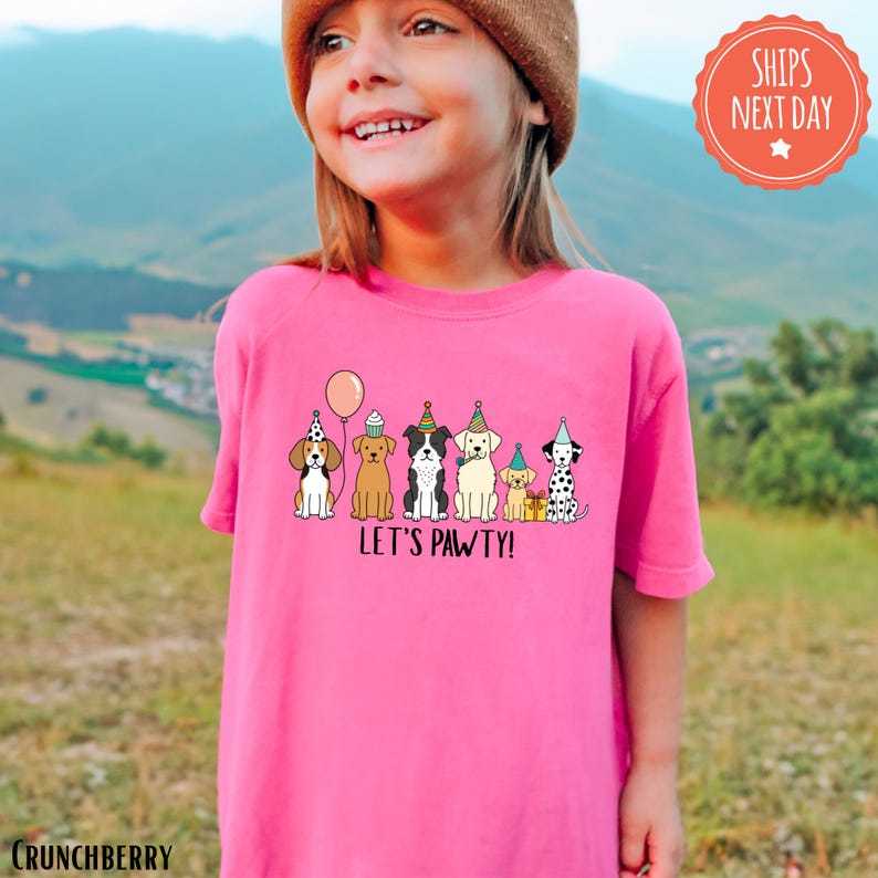 A young girl wearing a pink t-shirt with a graphic of cartoon dogs and the text "Let's Pawty!" smiling at the camera.