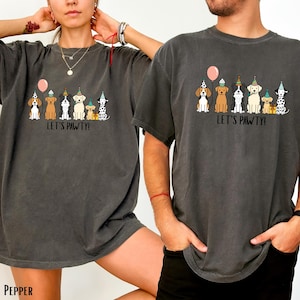 A woman and a man wearing gray t-shirts with a graphic design of dogs wearing party hats and the text "Let's pawty!"