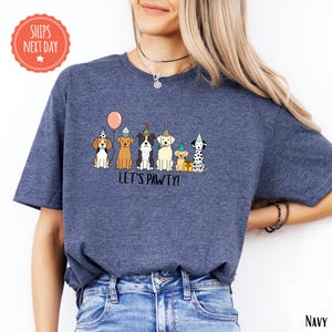 A woman wearing a navy blue t-shirt with a graphic of cartoon dogs wearing party hats and the text "Let's Pavement" printed on it.