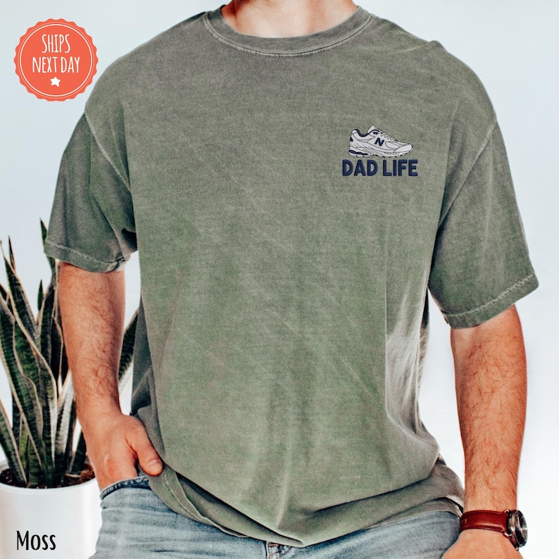a man wearing a dad life t - shirt next to a potted plant
