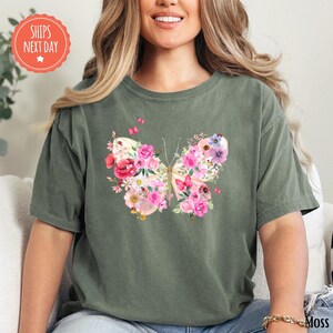 A woman wearing a green t-shirt with a colorful butterfly design on it, smiling and sitting on a couch.