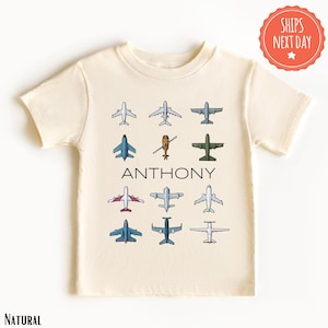 May include: A cream colored short-sleeved t-shirt with a graphic of various airplanes and the name "ANTHONY" printed in black.