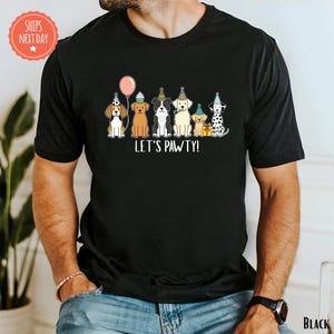A black t-shirt with a graphic design of six dogs wearing party hats and the text "Let's PAWTY!"