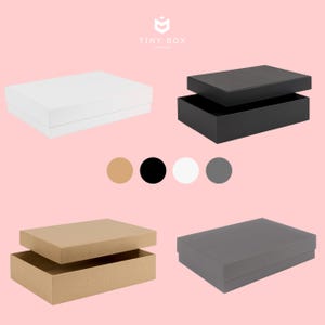May include: Four gift boxes with lids open. The boxes are white, black, brown, and grey. The boxes are all the same size and shape. The boxes are on a pink background. Tiny Box Company.