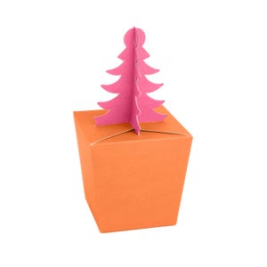 May include: An orange gift box with a pink paper Christmas tree on top. The tree is a cutout design with multiple layers. The box is square and has a simple, clean design, ideal for festive occasions.