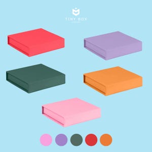 May include: Five colourful square boxes in red, purple, green, orange, and pink are displayed on a light blue background. The boxes are closed and have a simple, modern design. The Tiny Box Company logo is in the top right corner.