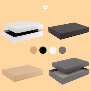 May include: Four gift boxes with lids in different colours: brown, black, white, and grey. The boxes are all the same size and shape, and they are arranged in a row.