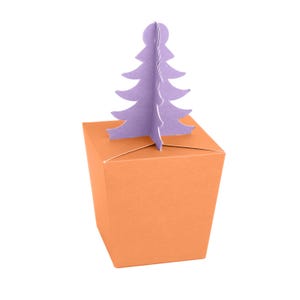 May include: An orange gift box with a lavender Christmas tree cutout. The box is square and has a lid. The tree is a simple, stylized design. The background is white.