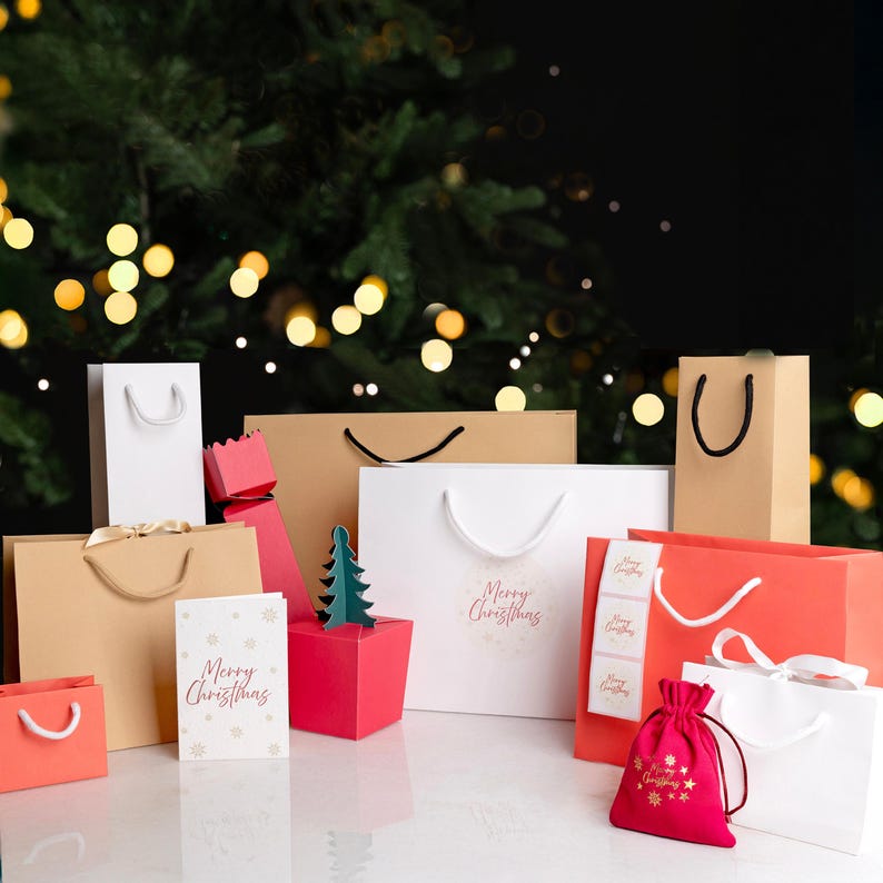 May include: A selection of Christmas gift bags and boxes in various sizes and colours, including white, red, and brown. Some bags have white rope handles. A red drawstring gift bag and a "Merry Christmas" card are also present.