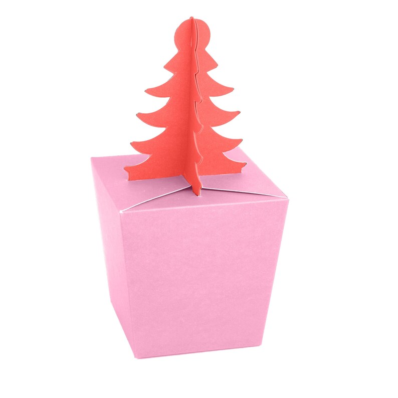 May include: A pink gift box with a red Christmas tree cutout. The box is a pale pink colour and has a square shape. The tree is a bright red colour and is made of cardboard.