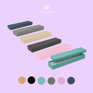 May include: Six rectangular boxes with lids, each in a different colour. The boxes are arranged in a row from left to right, with the lid of the last box open. The colours of the boxes are: navy blue, grey, beige, dark grey, pink, and teal.