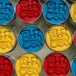 May include: Twelve small round tins with lids, each containing a different color play dough. The play dough is molded into the shape of a train engine. The lids of the tins have a label with the text "Choo Choo... Caleb Turns Two!" and a small train engine graphic.