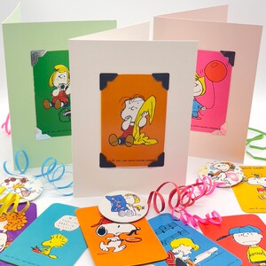 Pu&ograve; includere: Biglietti di auguri con personaggi dei Peanuts, tra cui Linus, Lucy e Sally, con angoli decorativi. Sono visibili anche biglietti e bottoni aggiuntivi con Snoopy e Woodstock. I biglietti sono in vari colori, con nastri decorativi.