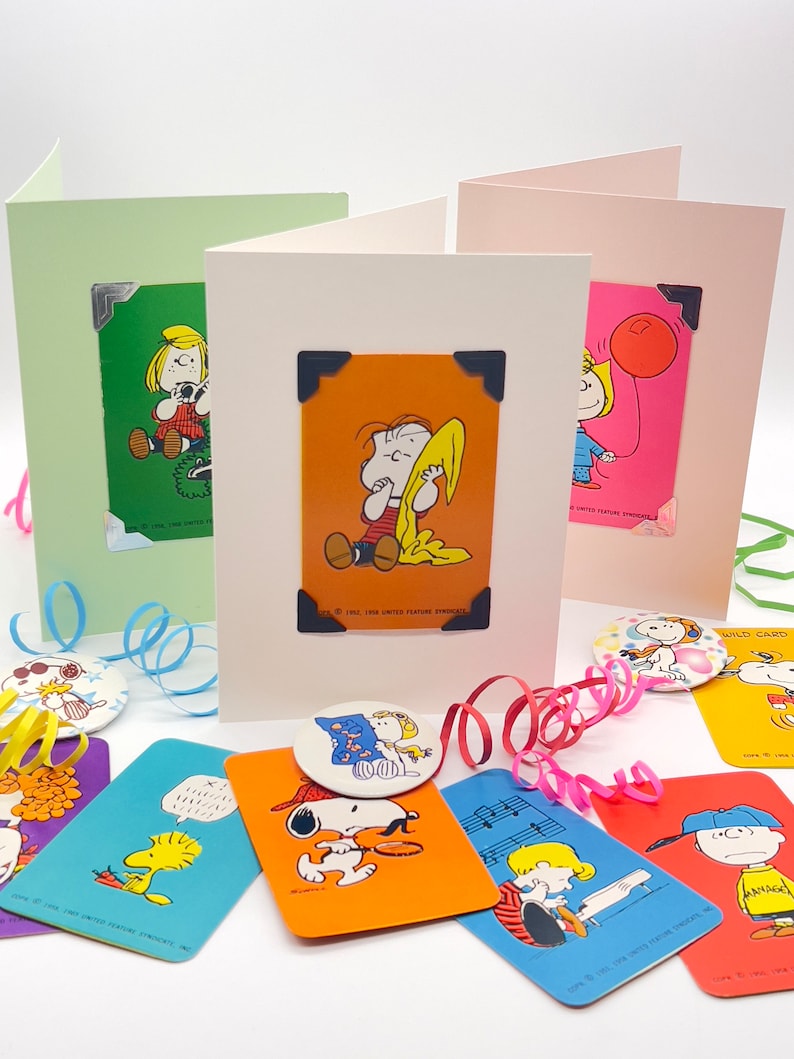 Pu&ograve; includere: Biglietti di auguri con personaggi dei Peanuts, tra cui Linus, Lucy e Sally, con angoli decorativi. Sono visibili anche biglietti e bottoni aggiuntivi con Snoopy e Woodstock. I biglietti sono in vari colori, con nastri decorativi.