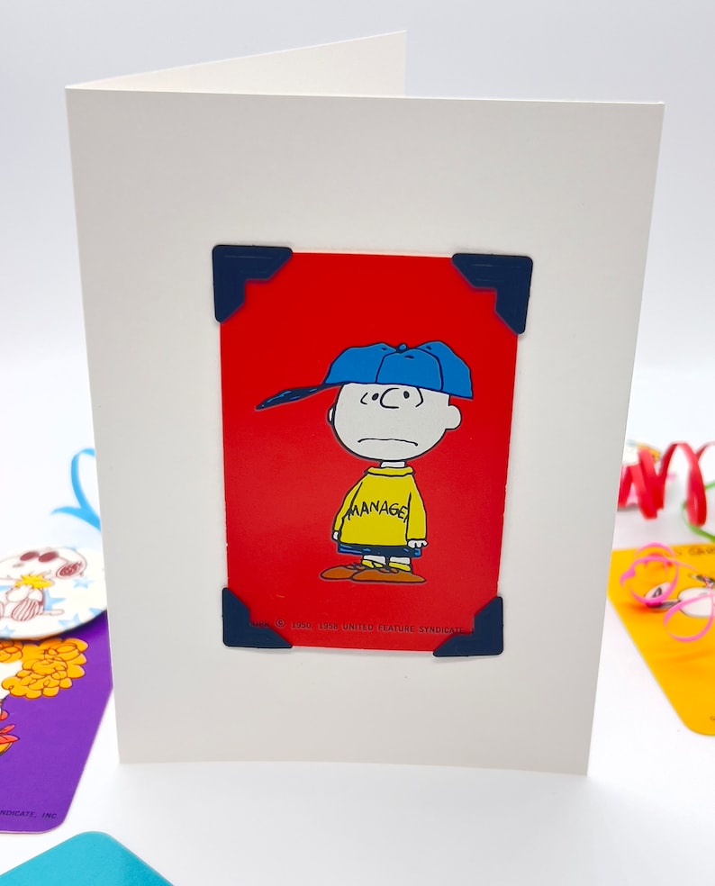 White card with red playing card featuring Charlie Brown with his baseball cap on and his classic yellow jumper with word Manager across it.