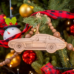 May include: A wooden Christmas ornament shaped like a classic car. The ornament is a light brown color and has a detailed outline of the car. The ornament is hanging on a Christmas tree with red and black plaid ribbon and brown wooden beads.