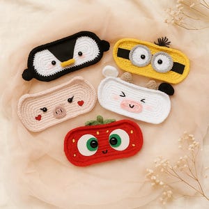 May include: A collection of handmade crochet sleep masks in various animal designs. The masks include a penguin, a minion, a pig, a cow, and a strawberry. Each mask features detailed facial features and vibrant colors, perfect for a fun and cozy sleep experience.