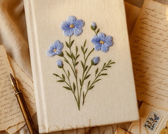 Può includere: Diario color crema con un design floreale ricamato a mano. Il ricamo presenta fiori blu con centri gialli e steli verdi. Una penna in stile vintage e lettere antiche sono disposte attorno al diario.