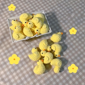 May include: A collection of yellow crocheted chicks, some in a white wire basket and others scattered on a checkered tablecloth.
