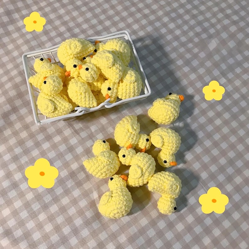 May include: A collection of yellow crocheted chicks, some in a white wire basket and others scattered on a checkered tablecloth.