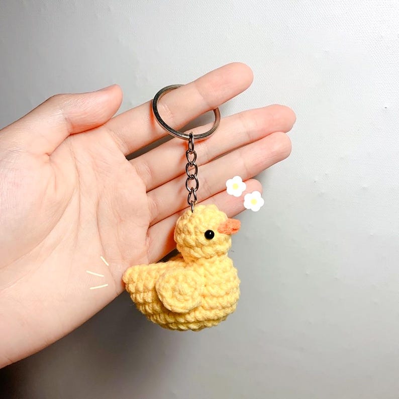 May include: A yellow crocheted duck keychain with a silver key ring and chain.