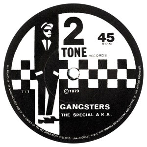 Puede incluir: Etiqueta de disco de vinilo de 45 RPM en blanco y negro con el texto "2 Tone Records" y "Gangsters The Special A.K.A." La etiqueta presenta un patrón a cuadros y la silueta de una persona con sombrero y traje.