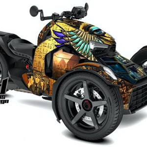 Puede incluir: Una motocicleta negra de tres ruedas con una envoltura gráfica de temática egipcia en oro, azul y verde. El gráfico presenta jeroglíficos, un ojo de Horus y una pirámide.