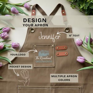 May include: A brown apron with leather accents and the text "Jennifer" in white script. The apron features pockets, a logo that says "The Riverbend Greenhouse", and the text "Design Your Apron". The apron is surrounded by purple tulips.