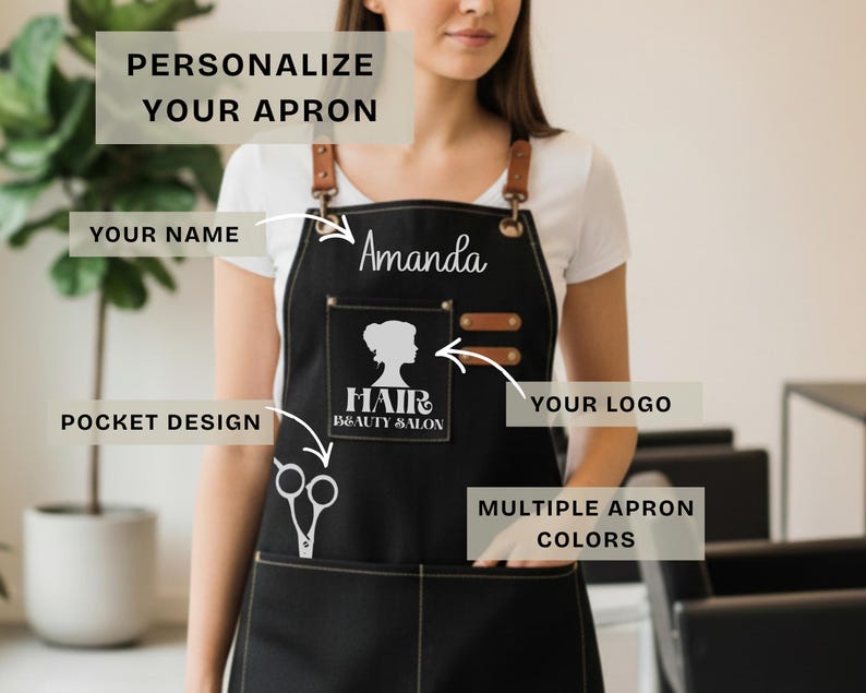 May include: Black apron with leather straps and pockets. The apron has the name "Amanda" in white script. A pocket features a silhouette of a woman's face and the words "Hair Beauty Salon". The apron is designed for personalization.