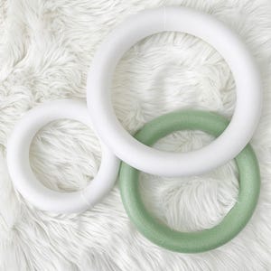 Puede incluir: Tres anillos de corona de espuma, uno blanco y dos verdes, sobre una superficie blanca y esponjosa.
