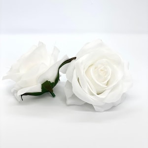 Könnte beinhalten: Zwei weiße künstliche Rosen mit grünen Stielen. Die Rosen sind geschlossen und haben eine weiche, samtige Textur.