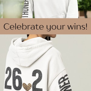 May include: White hoodie with a black and white graphic of "26.2" with a leopard print heart on the back. The left sleeve has the word "Marathoner" printed vertically in black and white.