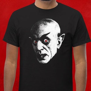 May include: A black t-shirt with a white graphic of a vampire with red eyes. The vampire is looking directly at the viewer.