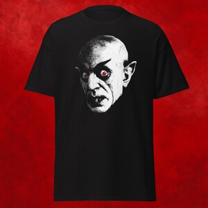 May include: Black t-shirt with a white image of a vampire with red eyes.