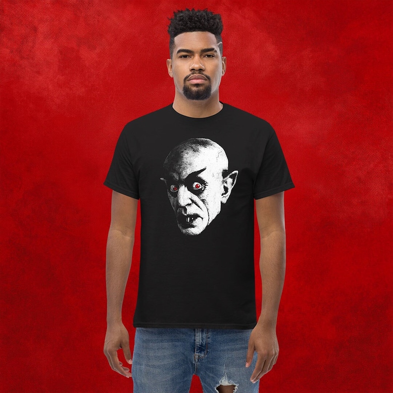 May include: A black t-shirt with a white graphic of a vampire with red eyes. The vampire is looking directly at the viewer.