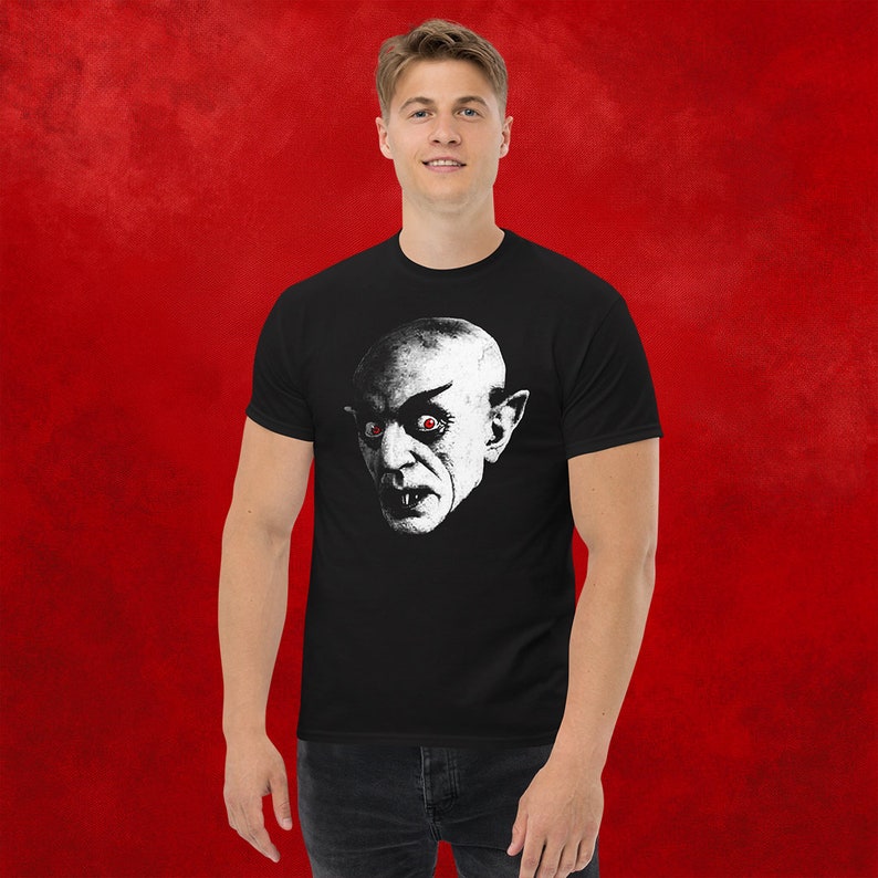 May include: A black t-shirt with a white graphic of a vampire with red eyes.