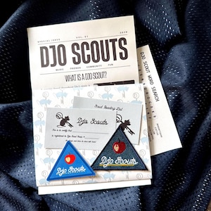 May include: A collection of Djo Scouts printed materials including a special issue booklet, a word search, and two cards, accompanied by two triangular embroidered patches featuring a red apple graphic and the text Djo Scouts in white script.